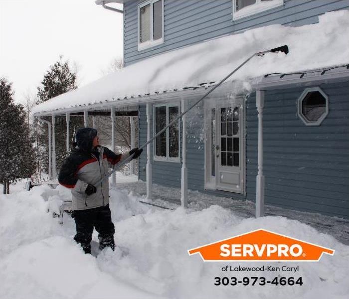 A person removes snow from their roof using a roof rake. 