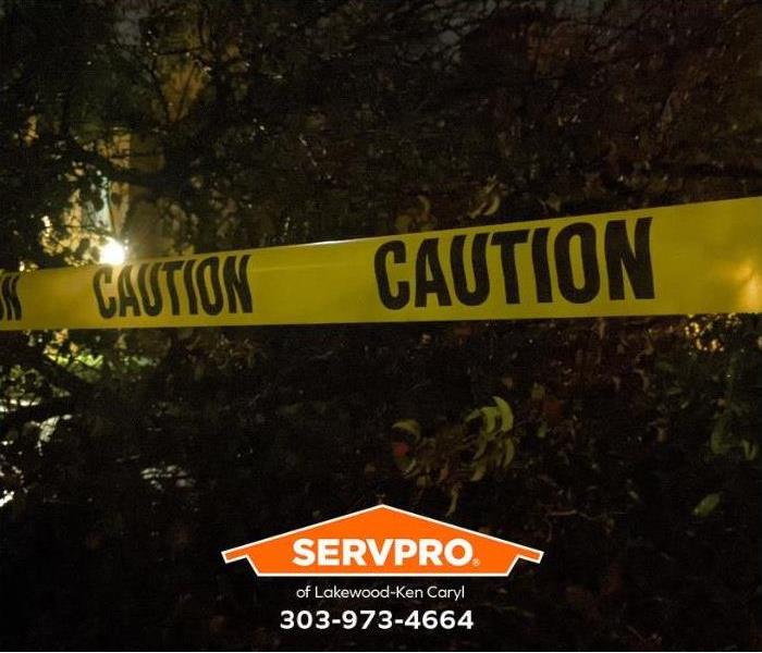 Caution tape prohibits entry into an area where a tree has fallen on a building at night.